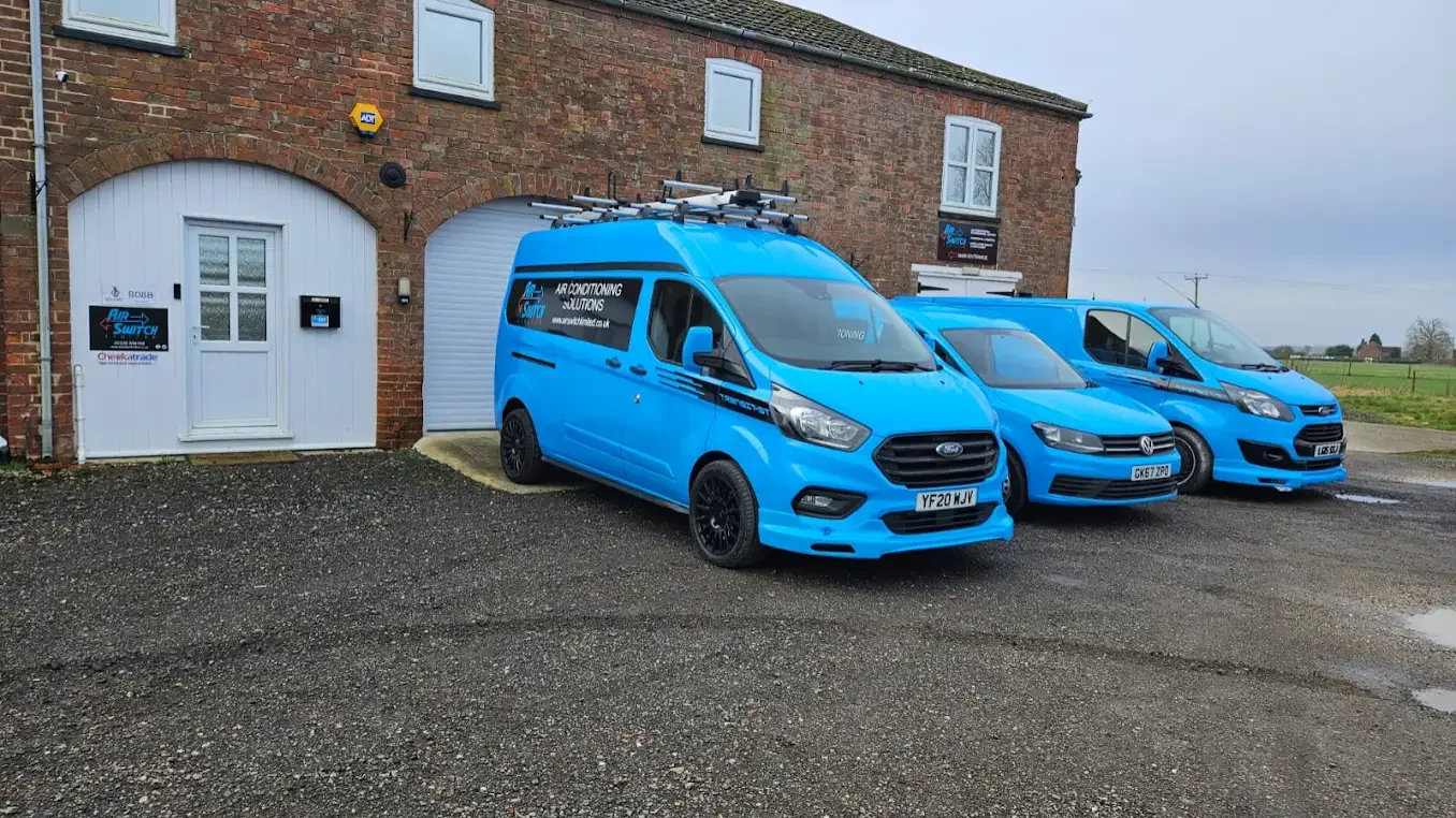 Three blue Air-Switch vans parked outside a brick building with white windows and doors.