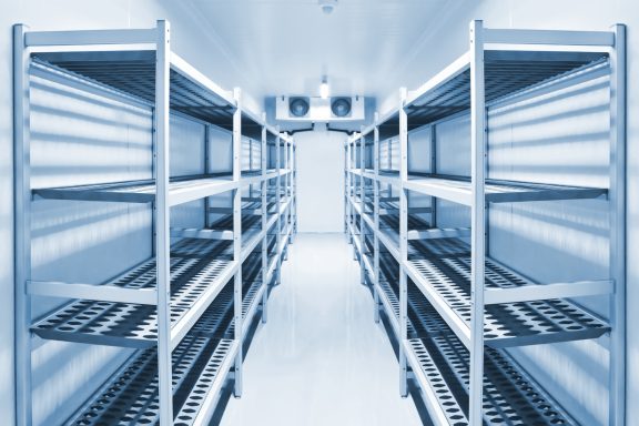 Empty metal shelving units in a large mobile refrigerated trailer unit with L.E.D lighting.