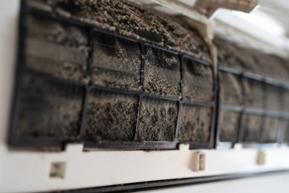 Dusty air conditioner filter showing accumulated dirt and debris in the mesh grid
