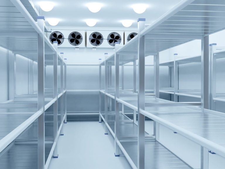 Empty clean chilled storage room with metal shelves and overhead evaporator units.