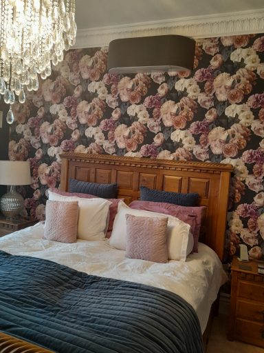 A classy and cosy bedroom with a floral wallpaper and chandelier style light with Toshiba Haori in dark grey above wooden head board