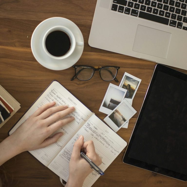 Business Support Colleague Picture of desk, hands and spectacles off with coffee to side whilst hands are making note in notebook