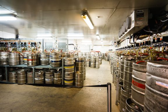 A brewery storage area filled with stacked beer kegs and metal shelves.