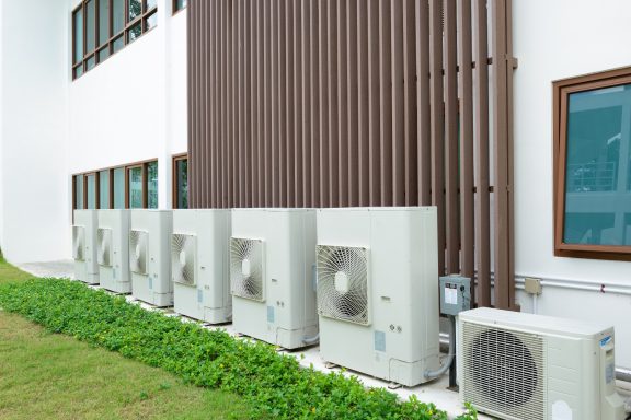 Row of external air source heat pump units and single air conditioning condenser unit